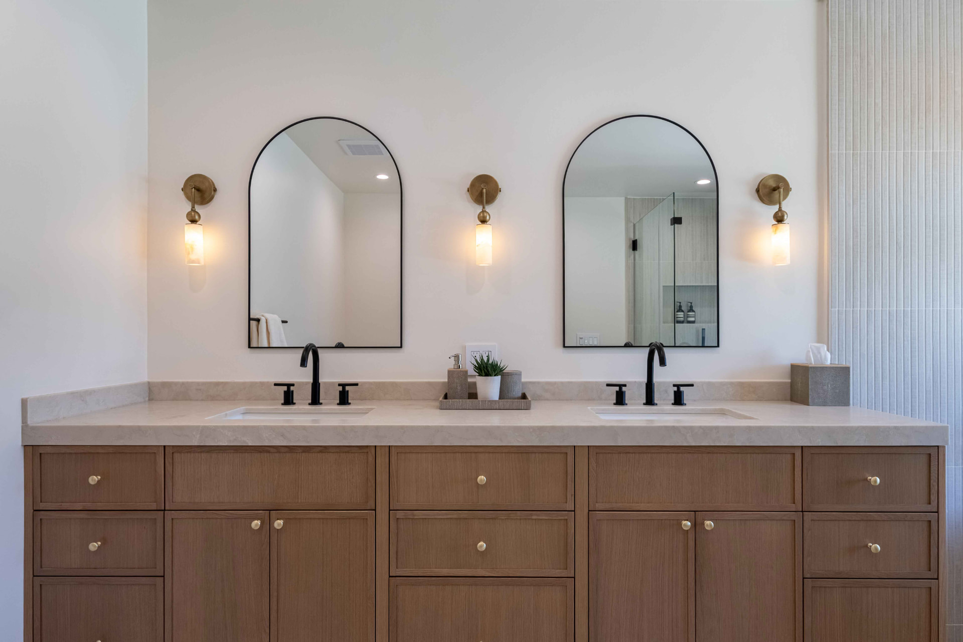 Primary bath with double vanity, arched mirrors, and brass sconces